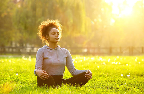 Women sitting cross-legged outside in nature on grass with sunlight